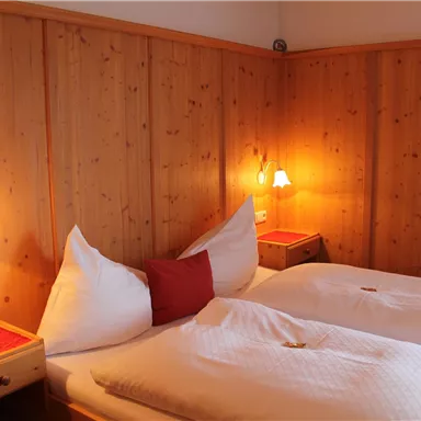 A cozy bedroom with two single beds and wooden walls. There are light sources on the walls that create a warm atmosphere.