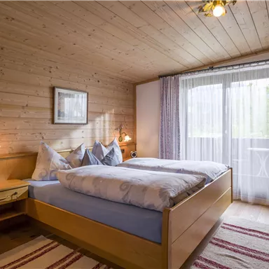 A cozy bedroom with wooden paneling and two beds. Large windows let in plenty of light and provide a view outside.