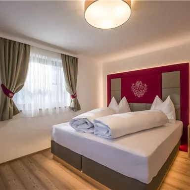A modern bedroom with a double bed and two pillows. A television is hanging on the wall, and the windows are adorned with curtains.