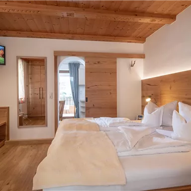 Ein modernes Schlafzimmer mit Holzvertäfelung und einem großen Doppelbett. Der Raum ist freundlich eingerichtet und hat einen Fernseher sowie einen großen Spiegel.