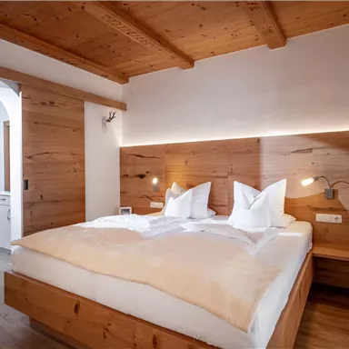 Ein gemütliches Schlafzimmer mit einem großen, hölzernen Bett und modernem Design. Die warmen Holzfarben sorgen für eine einladende Atmosphäre.