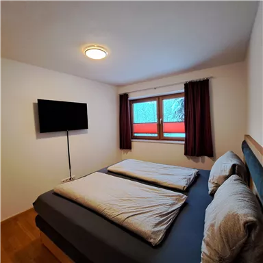 A cozy bedroom with two beds and a television. The window offers a view of the winter landscape.