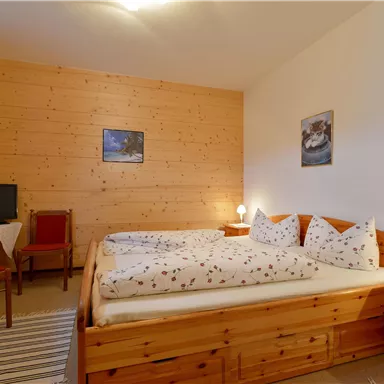 A cozy bedroom with wooden paneling and a double bed. There is a table, chairs, and a TV in the corner.