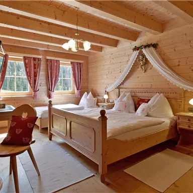 Ein gemütliches Schlafzimmer mit Holzwänden und einem großen Bett. Durch die Fenster fällt viel Tageslicht und der Raum ist rustikal eingerichtet.