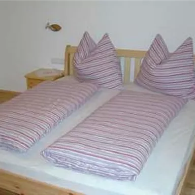 Ein einfaches Schlafzimmer mit einem Doppelbett und gestreiften Bettdecken. Die Kopfkissen sind hoch und spitz, und der Boden ist aus Holz.