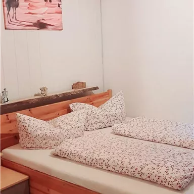 Ein gemütliches Schlafzimmer mit einem hölzernen Bett und passenden Kissen. An der Wand hängt ein Bild von Kamele in der Wüste.