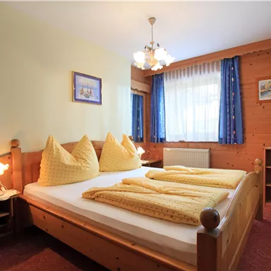 A cozy bedroom with a double bed and yellow blankets. Bright windows and wood paneling give the room an inviting atmosphere.