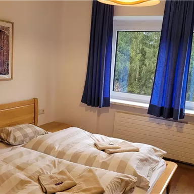 A cozy bedroom with two beds and a large window. The blue curtains and the artwork on the wall create an inviting atmosphere.