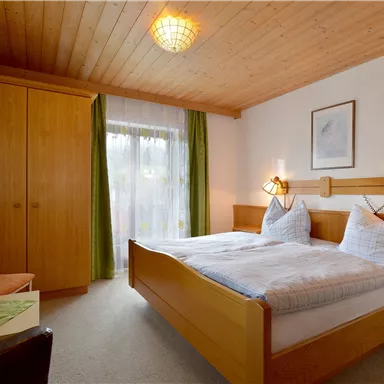 A cozy bedroom with two beds and light wood decor. Generous windows let in plenty of light and give the room an inviting atmosphere.