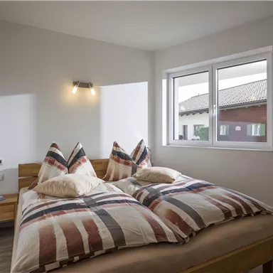 Ein gemütliches Schlafzimmer mit einem Doppelbett und karierten Bettdecken. Das Fenster bietet einen Blick nach draußen auf ein ruhiges Wohngebiet.