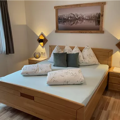 A cozy bedroom with a large wooden bed and modern nightstands. Soft lighting and landscape pictures create an inviting atmosphere.