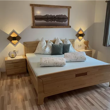 A modern bedroom with a large wooden bed and pillows. Soft lighting creates a cozy atmosphere.