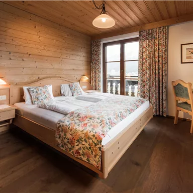 A cozy bedroom with wood paneling and two beds. The room is friendly and inviting, with a table and windows that let in plenty of light.