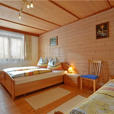 A cozy bedroom with two wooden beds. The walls are made of wood, and there are large windows for plenty of daylight.