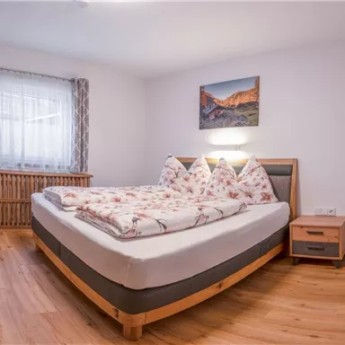 A modern bedroom with a large bed and cozy pillows. The room has hardwood flooring and a windowsill with a beautiful view.