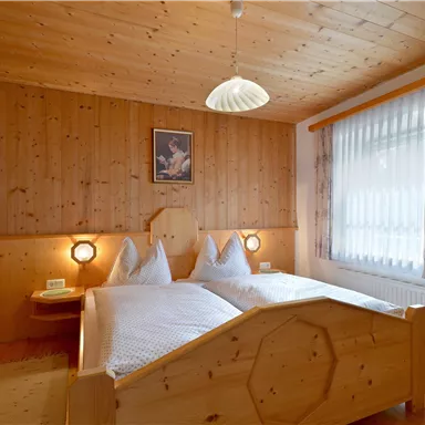 A cozy bedroom with wood paneling and two single beds. Soft lighting and a window create an inviting atmosphere.