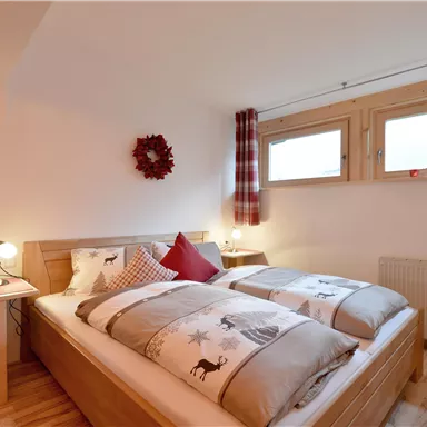 Ein gemütliches Schlafzimmer mit einem Doppelbett und Holzverkleidungen. Es gibt zwei Fenster, die für Tageslicht sorgen, und eine Weihnachtsdekoration an der Wand.