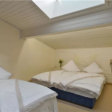 Ein gemütliches Schlafzimmer mit zwei Betten und hellen Bettwäsche. Das Zimmer hat eine abgesenkte Decke und ein Oberlicht, das Licht hineinlässt.
