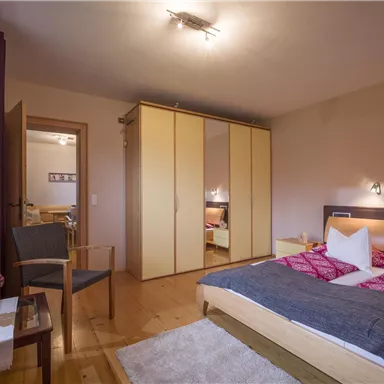 Ein gemütliches Schlafzimmer mit einem großen Bett und einem Kleiderschrank. Der Raum ist hell und einladend, mit einem Stuhl und einem kleinen Tisch.