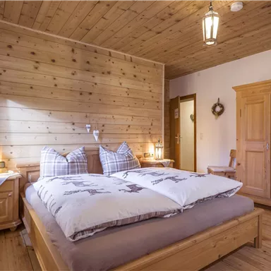 A cozy bedroom with wooden decorations and warm light. The room is equipped with a double bed and a wooden wardrobe.