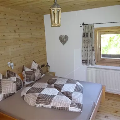 A cozy bedroom with wooden paneling and a large bed. The windows let in plenty of daylight and create an inviting atmosphere.