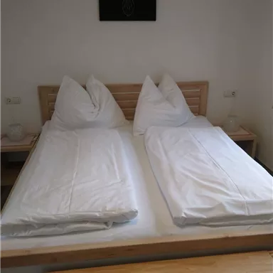 A simple bedroom with two single beds and white bedspreads. A picture of a deer head hangs on the wall.