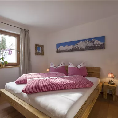 Ein gemütliches Schlafzimmer mit einem großen Bett und rosa Bettwäsche. Das Fenster bietet einen Blick auf schöne Pflanzen und eine Berglandschaft an der Wand.