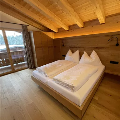A cozy bedroom with wooden walls and a large bed. Large windows provide a view outside.