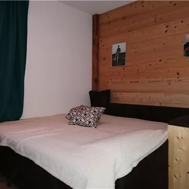 A cozy bedroom with a large bed and wooden paneling. Curtains hang in front of a window, and photos are mounted on the wall.