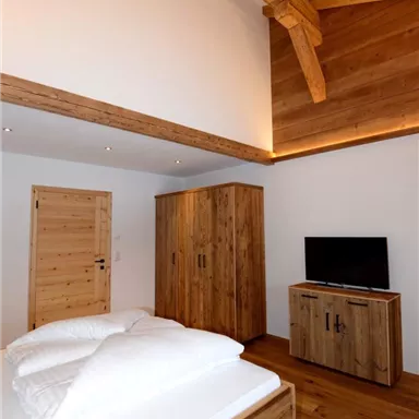A modern bedroom with wooden floors and wooden furniture. The walls are light, and a large window area provides plenty of light.