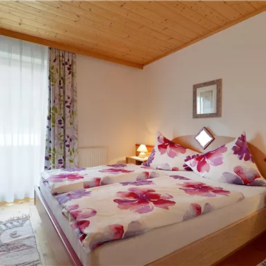 A cozy bedroom with a double bed and colorful floral patterns. The room design is bright and inviting, with soft light from the table lamps.