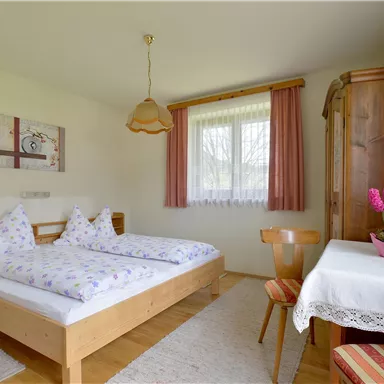 Ein gemütliches Schlafzimmer mit zwei Betten und einem Tisch. Der Raum hat große Fenster, die viel Tageslicht hereinlassen.
