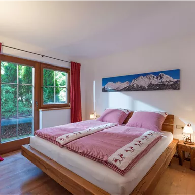 Ein gemütliches Schlafzimmer mit zwei Betten und gemütlicher Bettwäsche. Ein großes Fenster lässt natürliches Licht hinein und bietet Blick ins Grüne.