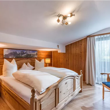 Ein gemütliches Schlafzimmer mit einem Holzbett und hellen Kissen. Große Fenstertüren sorgen für viel Tageslicht und bieten einen schönen Blick nach draußen.