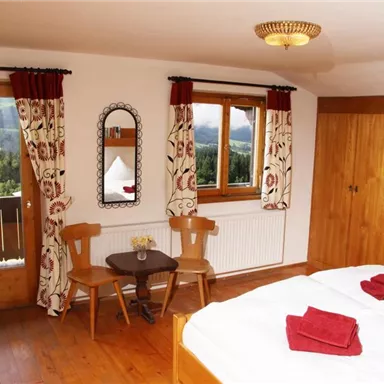 A cozy bedroom with wood decoration and large windows. Two chairs and a table complement the pleasant atmosphere.