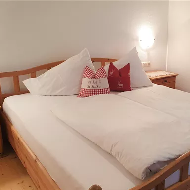 A cozy bedroom with a large double bed and bright pillows. There are wooden furniture and soft lighting.