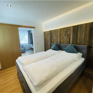 A modern bedroom with a double bed and wood paneling. The room is designed to be bright and cheerful.