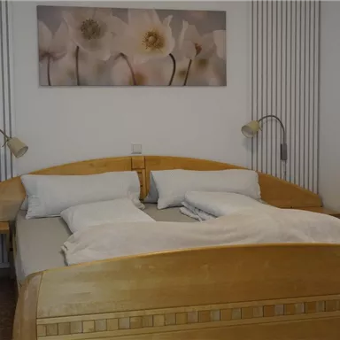 Ein gemütliches Schlafzimmer mit einem Doppelbett aus Holz. An der Wand hängen Bilder von Blumen, und es gibt zwei Leselampen auf beiden Seiten des Bettes.