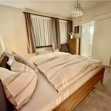 A cozy bedroom with a double bed and soft pillows. The room is brightly lit and has curtains as well as a wardrobe.