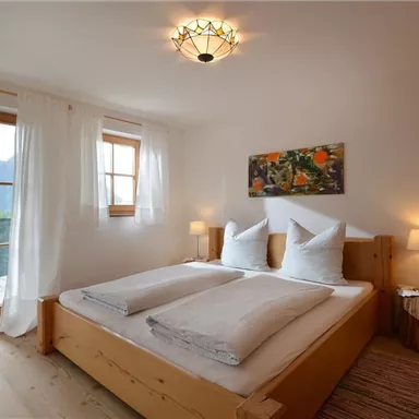 A cozy bedroom with two beds and large windows offering a view of the mountains. The decor is bright and inviting, featuring wooden details and soft lighting.