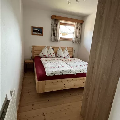 Ein gemütliches Schlafzimmer mit einem Doppelbett und Holzdesign. Die Wände sind hell gestrichen und ein Fenster sorgt für Tageslicht.