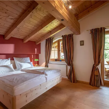 Ein gemütliches Schlafzimmer mit Holzbalkendecke und einem großen Fenster. Das Zimmer ist hell und einladend, mit einem Doppelbett und warmen Farben.