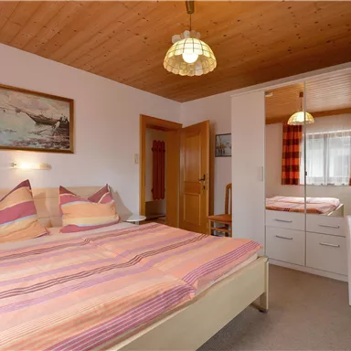 A cozy bedroom with a double bed and colorful pillows. In the background, a mirror and wooden ceiling can be seen.