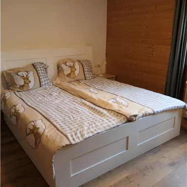 A cozy bedroom with a double bed and wooden paneling. The bedding is in soft colors with an animal motif.