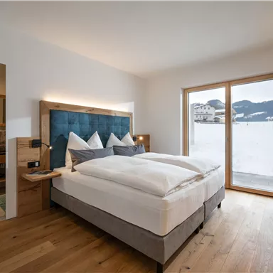 A modern bedroom with a large bed and cozy furnishings. Large windows offer a view of the snowy landscape.