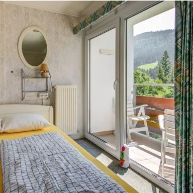 Ein gemütliches Schlafzimmer mit einem Doppelbett und einem Balkon mit Aussicht auf die Berge. Das Zimmer hat eine helle, freundliche Dekoration und große Fenster für viel Tageslicht.