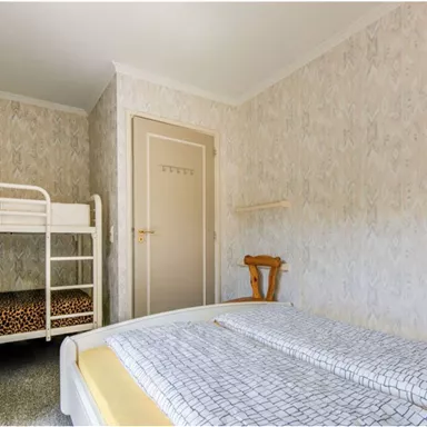 Ein einfaches Schlafzimmer mit einem Etagenbett und einem Einzelbett. Die Wände sind mit einem gemusterte Tapete dekoriert.