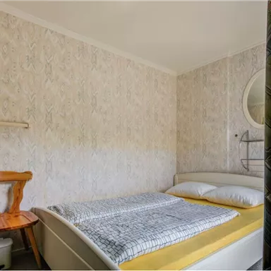 Ein einfaches Schlafzimmer mit einem Bett, einem Stuhl und hellen Wänden. Die Einrichtung ist modern und minimalistisch.