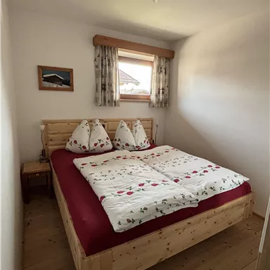 Ein gemütliches Schlafzimmer mit einem großen Bett, das mit roten und weißen Bettbezügen dekoriert ist. Das Zimmer hat einen hellen, freundlichen Charme mit Holzdetails und einem Fenster.