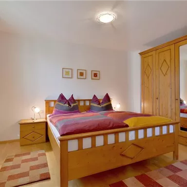 A cozy bedroom with a large bed and wooden cabinets. The walls are bright and the windows let in a lot of light.